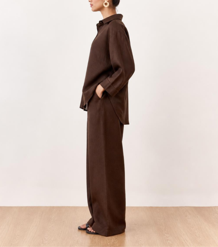Side view of woman wearing brown linen co-ord set with hand in pocket and sandals