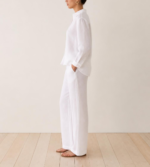 Side view of woman wearing white linen co-ord set with hand in pocket and flat sandals
