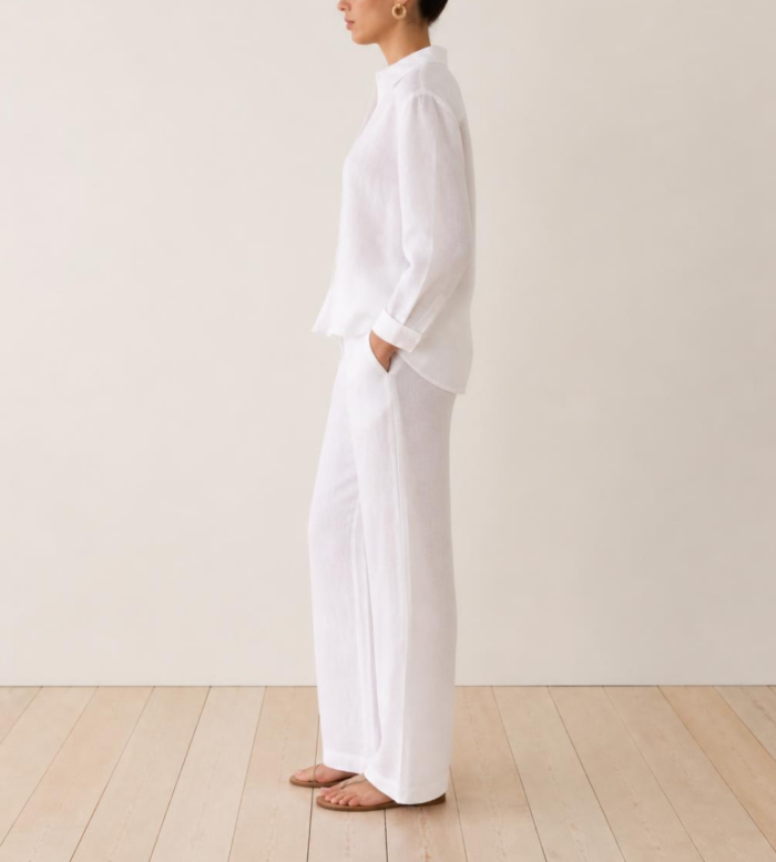 Side view of woman wearing white linen co-ord set with hand in pocket and flat sandals