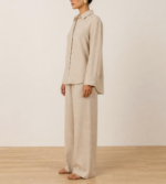 Side view of woman wearing beige linen co-ord set with buttoned shirt, wide-leg trousers and flat sandals