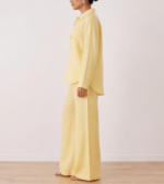 Side view of woman wearing butter yellow linen co-ord set with wide-leg trousers and flat sandals